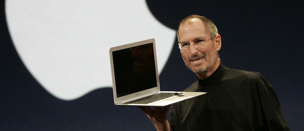 business model of apple - Steve Jobs holding Macbook